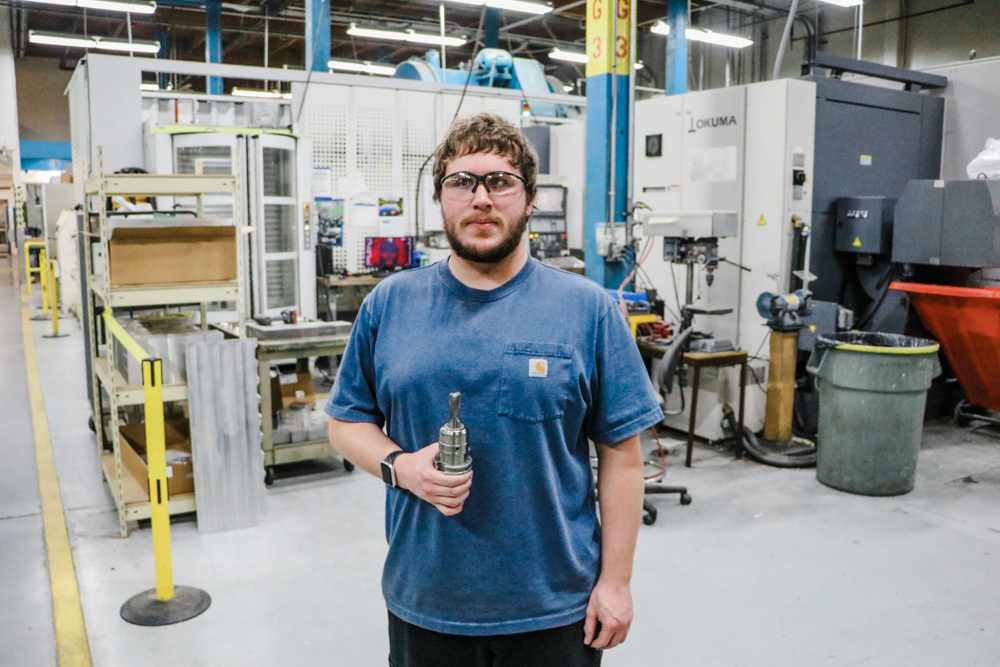 Machinist Alex Carter in front of a large Okuma CNC machine at the Seattle facility